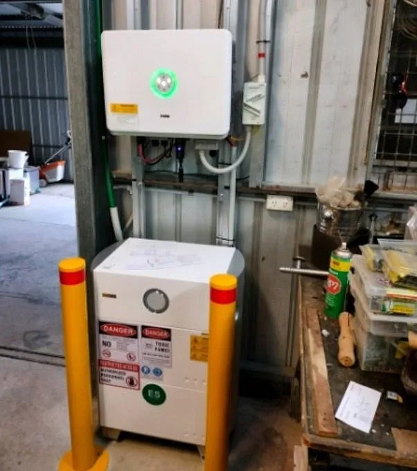 A white inverter and battery on a workshop wall with yellow bollards beside it