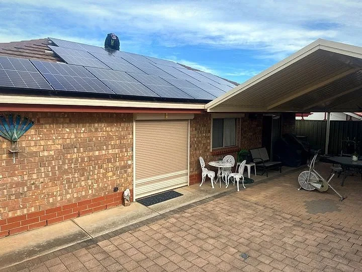 Solar panels on the tiled roof of a brick home beside a paved patio