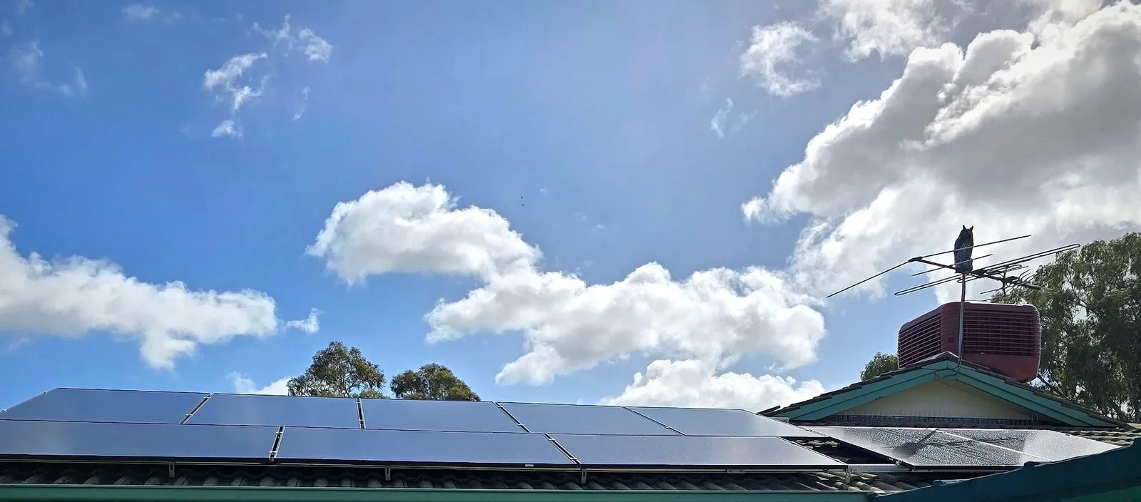 Solar panels along the roof edge of a brick home under a blue sky with clouds